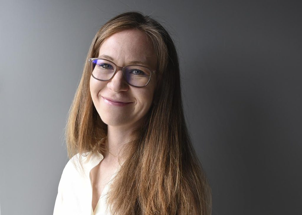 Marie Pihlström katsoo kameraan luonnonvalossa, hänellä on silmälasit ja pitkät ruskeat hiukset